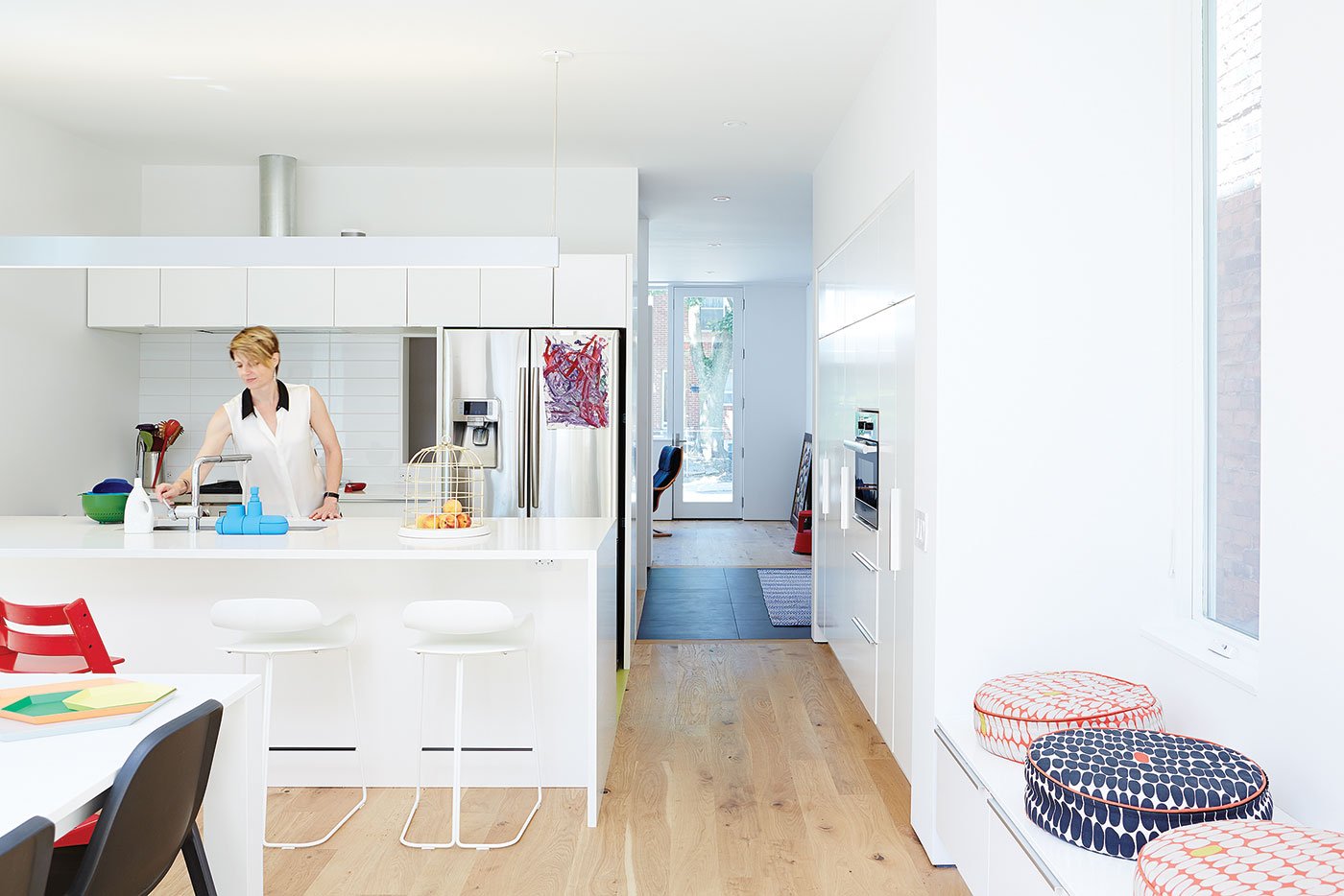 A female person is using the sink, the cabinetry is white and colourful object are visible