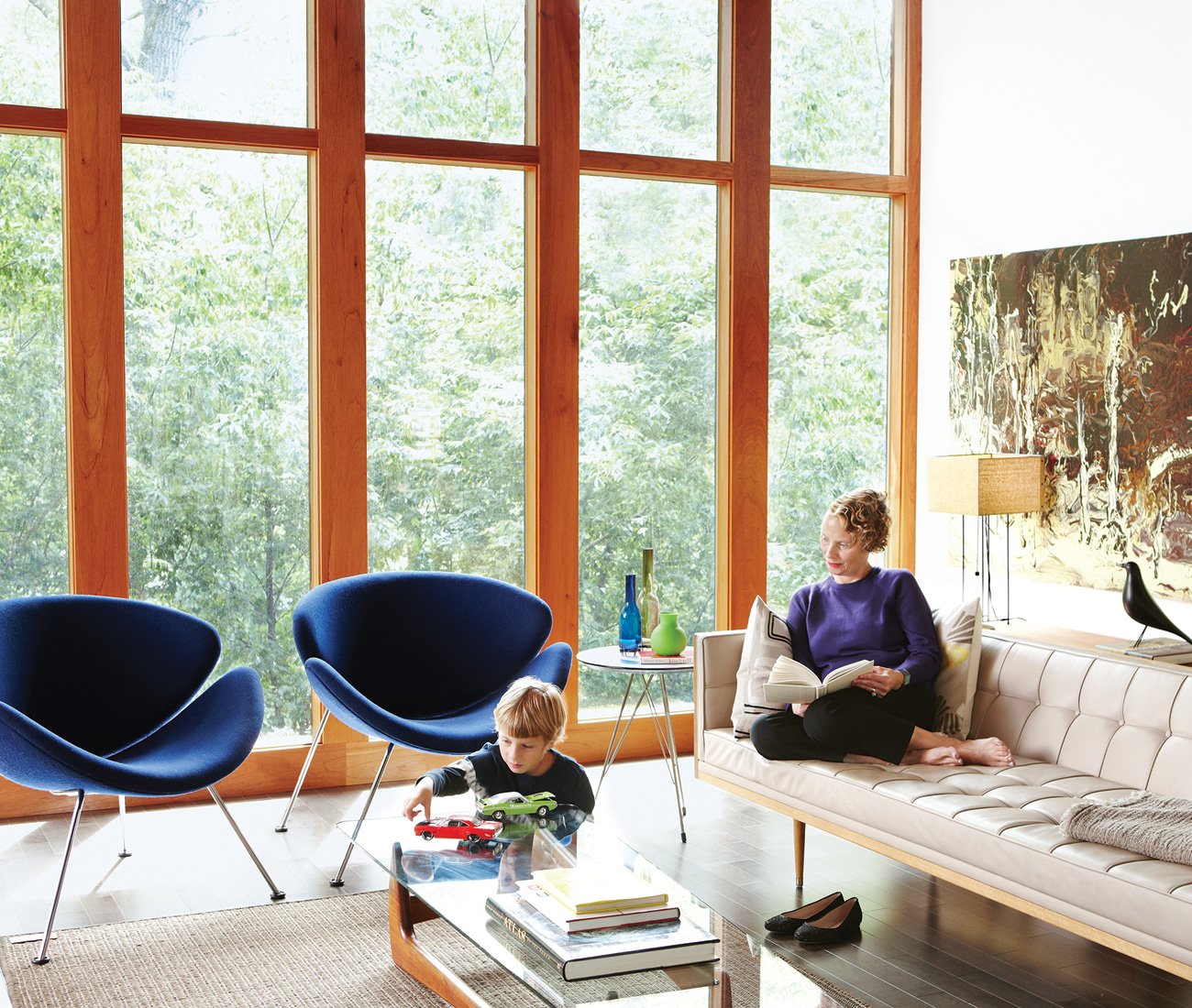 A woman is sitting on the couch while a kid is playing on the living room coffee table of a mid-century modern home