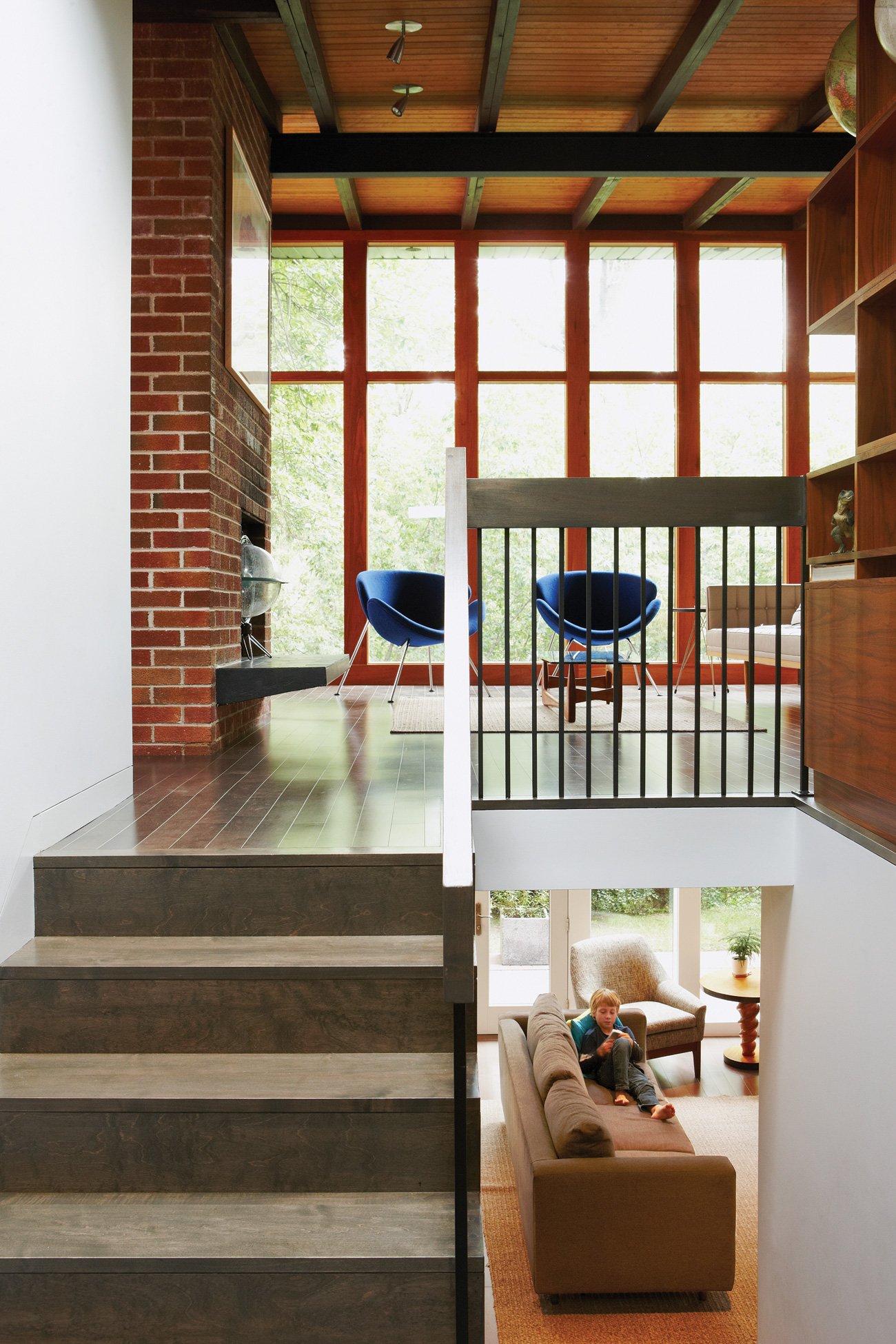Split level section of mid-century modern bungalow, a kid is visible on the house couch reading.