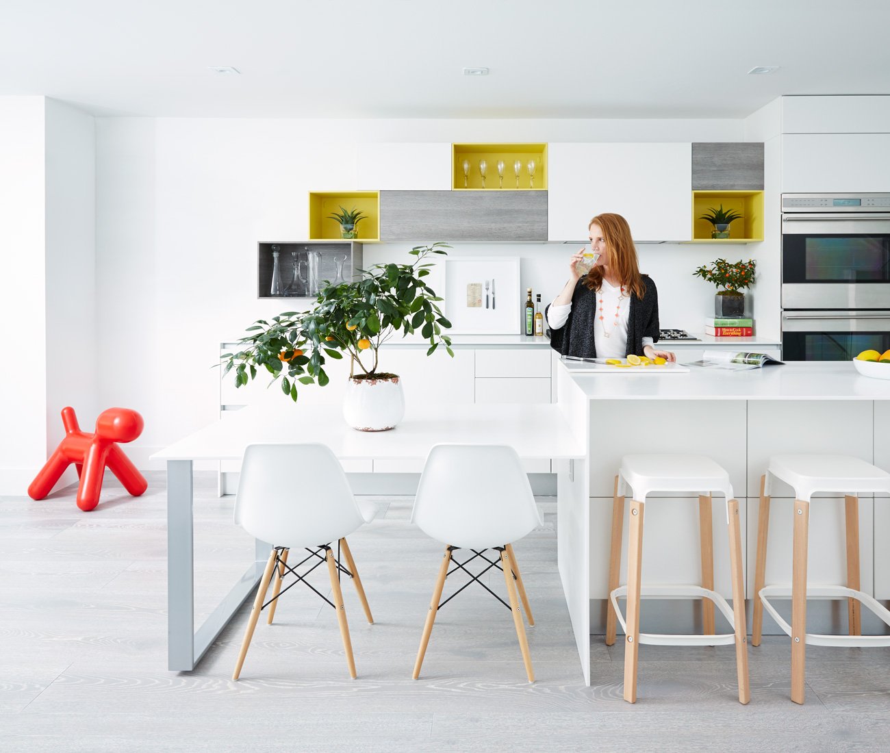 A female person is sipping from a glass while standing behind the island of a white kitchen | kitchen design ideas