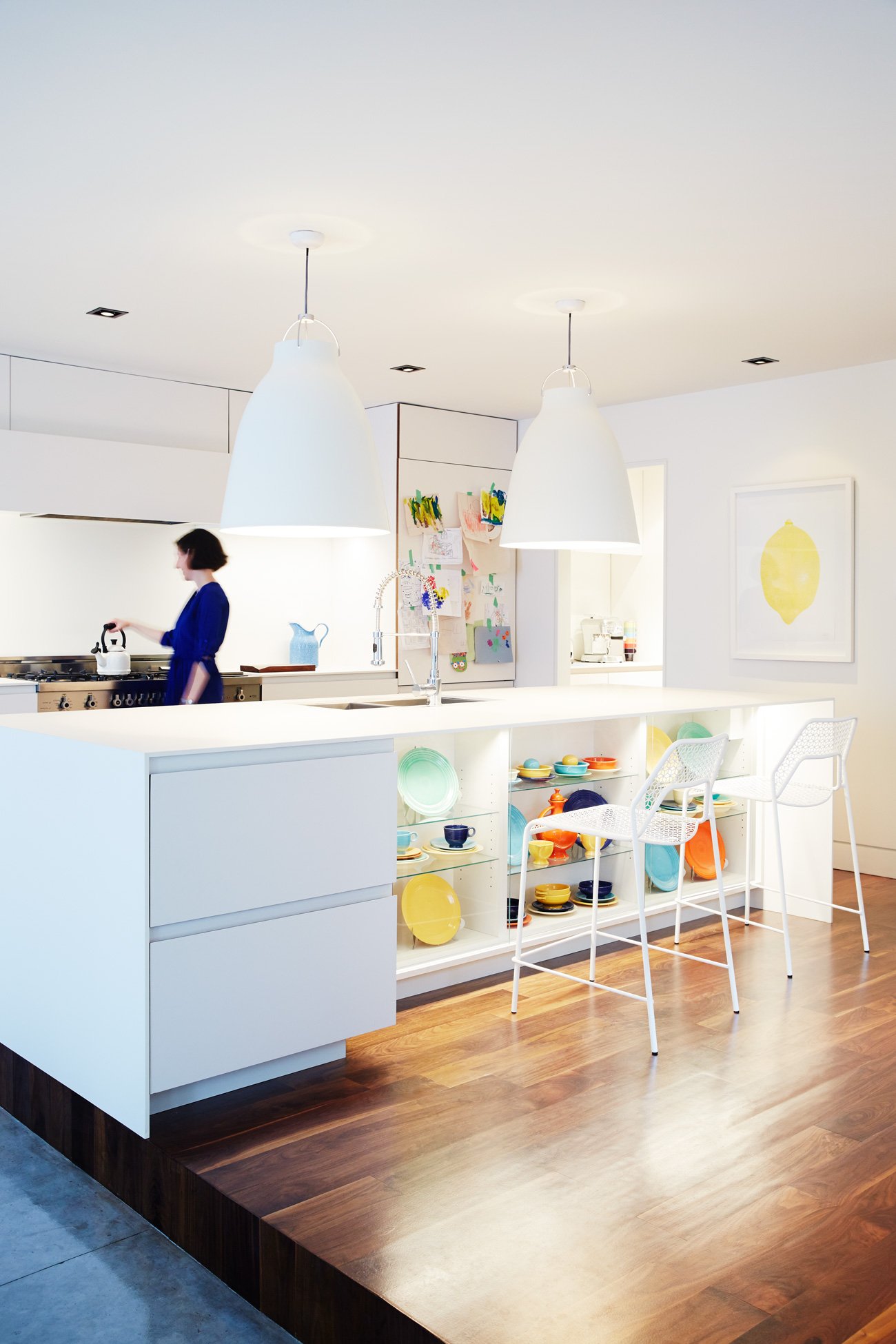 A female person is preparing the tea on the gas stovetop of a white kitchen. Colourful accessories are visible. | Kitchen Design ideas