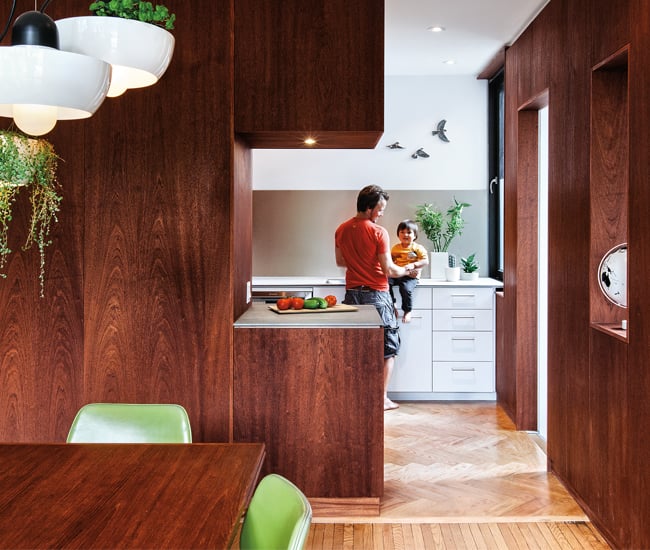 A male person is holding a baby sitting on the countertop