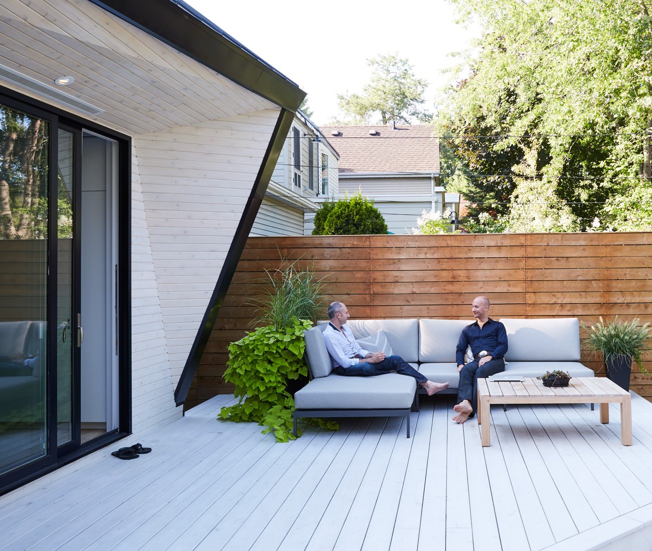 traditional homes modern additions, two men sitting on a couch on the backyard patio