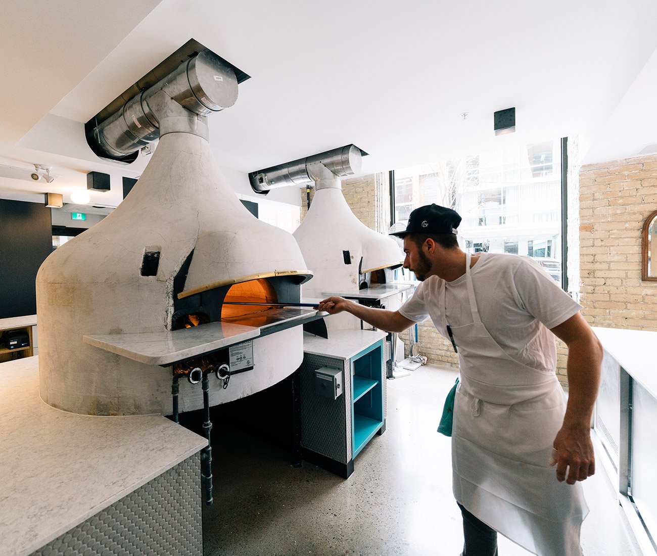 Pizza maker checking pizzas inside the massive hand-built white pizza ovens at General Assembly in Toronto.