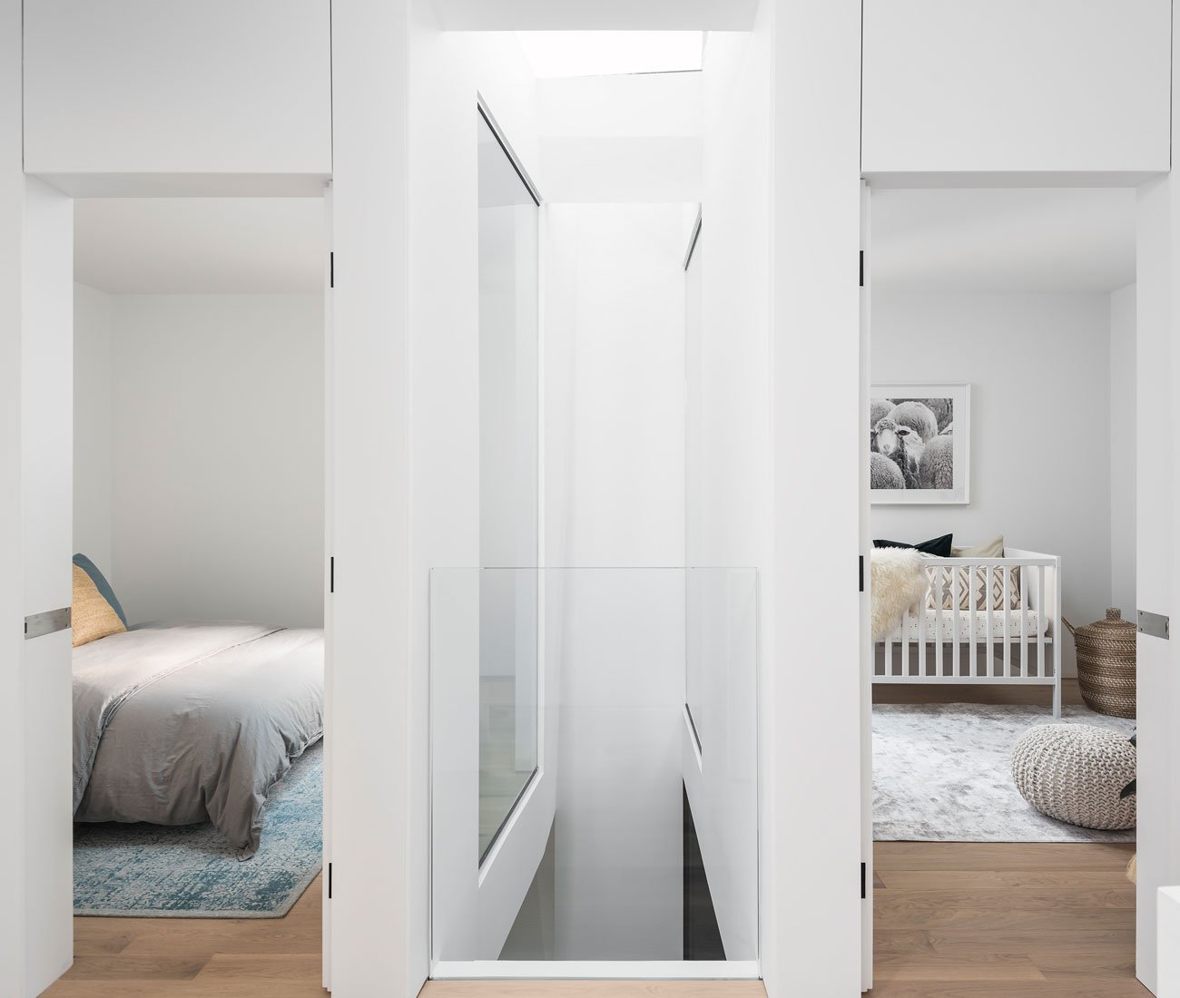 Phaedrus Studio Tesseract House Designlines Magazine Long Branch Home Top-floor landing with two sunlit bedrooms illuminated by an adjacent light well, featuring beds, area rugs, and a pouf from Ikea.