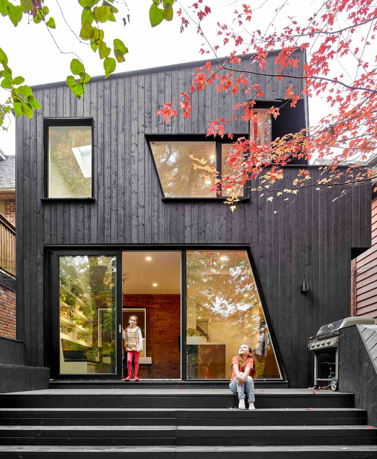Two kids are standing on the patio of a traditional house addition cladded in black wood.